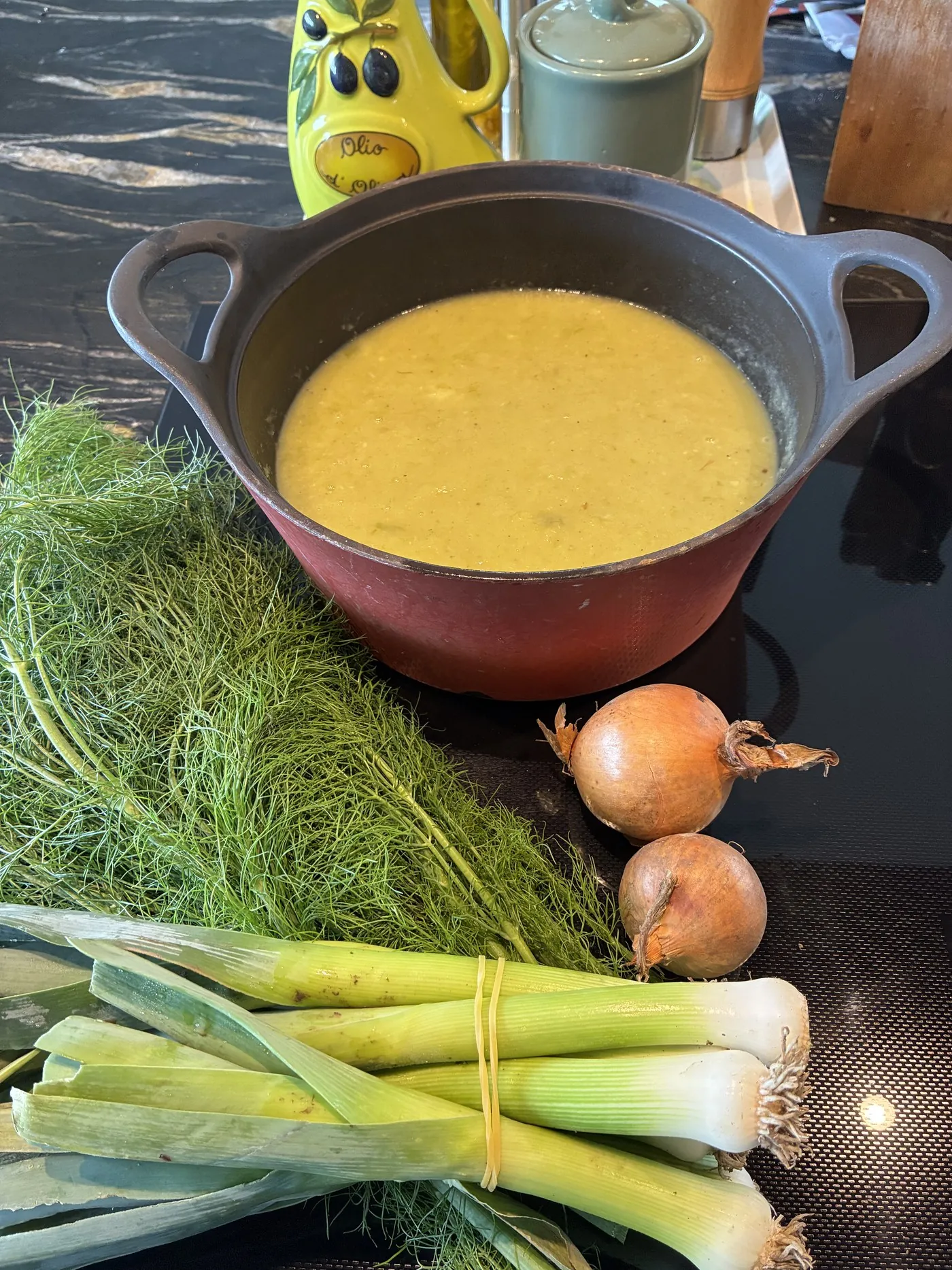 Open pan met verse soep op het fornuis, met prei, venkel en uien ernaast